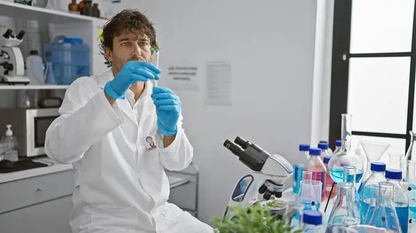 stock image Hispanic scientist with beard examines plant sample in bright laboratory, surrounded by equipment and microscope.