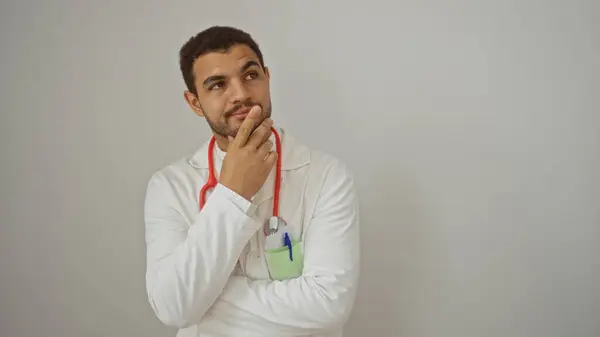 Stock image Young hispanic man isolated over white background with a thoughtful expression wearing a white lab coat and red stethoscope around his neck