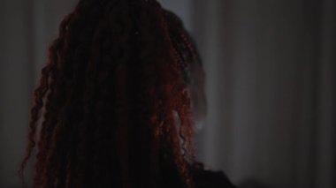 Sönük kırmızı bir odada örgülü siluetli bir kadın gizemli ve şüpheli bir atmosferi taşıyor..