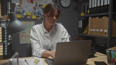 Stresli, genç bir İspanyol kadın dedektif ofis içi karmakarışık bir davada çalışıyor. Evrak, dizüstü bilgisayar ve kanıt gösteriyor..