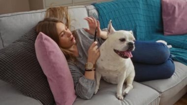 Genç, güzel bir kadın evcil köpeğiyle bir kanepede uzanıyor..