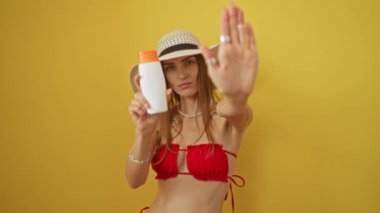 Bikinili kadın elinde güneş kremi tutuyor. El hareketi, ciddi ifade, izole edilmiş sarı arka planda kendine güveni olan savunma.