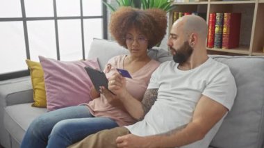 Modern oturma odasında tablet ve kredi kartı kullanarak internetten alışveriş yapan ırklar arası bir çift.