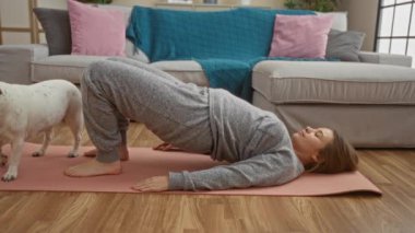 Sarışın, beyaz bir kadın köpeğiyle yoga yapıyor. Oturma odasında..
