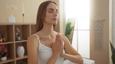 Güzel, genç bir kadın ellerini dua pozisyonunda bir spa sağlık odasında meditasyon yapıyor. Huzurlu ve rahatlatıcı kapalı alan ortamını kucaklıyor..