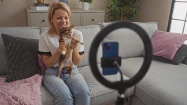 Chihuahua köpeğini tutan genç bir kadın oturma odasında bir video kaydediyor..