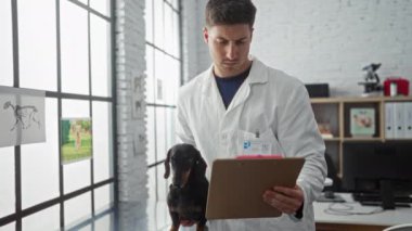 Veteriner kliniğinde tekel tutan Latin kökenli genç bir veteriner, duvarında köpek posterleri olan kapalı bir odada bir panoya bakıyor..
