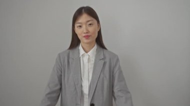 Ceketli genç Çinli kadın, ayakta duruyor ve el şeklinde kalp sembolü gösteriyor, izole edilmiş beyaz bir arka plan üzerinde romantik bir jest olarak.