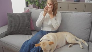 Genç bir kadın, dinlenen köpeğinin yanındaki kanepede hapşırır..