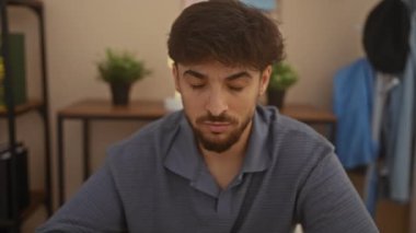 Oturma odasında sakallı genç bir adam. Modern dekorları ve çiçekleri var. Rastgele bir şekilde rahatlıyor..
