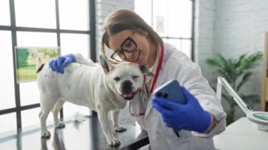 Veteriner kadın, büyük pencereli, parlak bir veteriner kliniğinde mutlu bir köpekle selfie çekiyor..