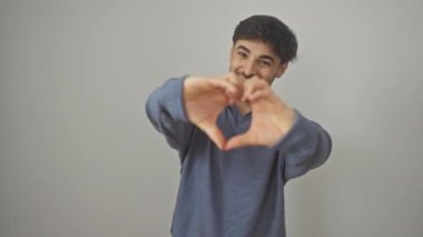 Gülümseyen genç Arap adam, yalnız başına duruyor, izole edilmiş beyaz bir arka planda, kalp şeklinde romantik bir sevgi gösteriyor.