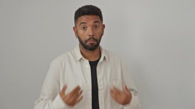 Hiçbir şeyden haberi olmayan Afro-Amerikan bir adam, gömlek giyiyor, kollarını kaldırmış, soyutlanmış beyaz bir arka plana karşı kafa karışıklığı ve şüphe gösteriyor.