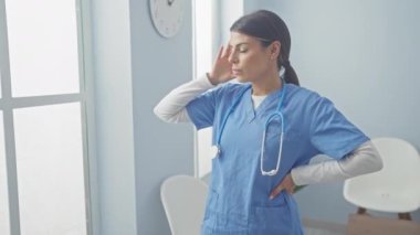 Önlüklü stresli bir kadın hemşire, parlak bir klinikte baş ağrısı çekiyor..
