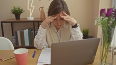 Ev ofis ortamında dizüstü bilgisayarı ve belgesi olan stresli bir kadın, aciliyet ve baskı hissi uyandırıyor..