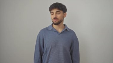 Ciddi genç Arap adam, basit, doğal bir ifadeyle duruyor, izole beyaz bir arka plan üzerinden doğrudan kameraya bakıyor.