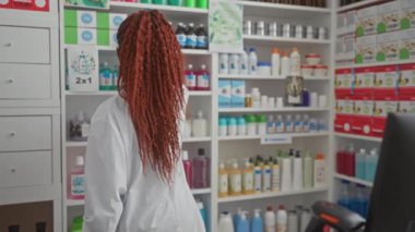 Modern bir eczanenin raflarında ilaç analizi yapan Afrikalı Amerikalı kadın eczacı..