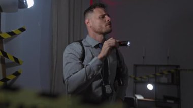 Odaklanmış bir dedektif, loş aydınlatılmış bir suç mahallini gece feneriyle araştırıyor..