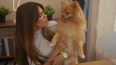 Güzel bir kadın Pomeranian köpeğini iyi aydınlatılmış, rahat bir oturma odasında tutuyor, sıcaklığını ve dostluğunu iletiyor..