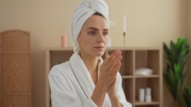 Kaplıca ortamında, kafasında havluyla beyaz bir bornoz giyerken kapalı bir sağlık merkezinde beyaz bir elbise giyen güzel bir kadın..