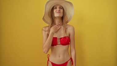 Yazlık şapkalı bir kadın boğazına dokunuyor, ağrı ve grip belirtileri gösteriyor, sarı arka planda izole edilmiş.