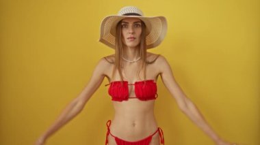 Bikinili ve yaz şapkalı kadın şaşırmış ve korkmuş ifadesiyle şok olmuştu. Elleri başının üstünde, ağzı açık, izole edilmiş sarı arka plandaydı. 