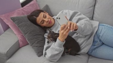 Genç bir İspanyol kadın evde Chihuahua 'sıyla rahat bir an geçirir, evdeki rahat bir kanepede selfie çeker..
