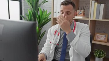Stresli doktor beyaz önlüklü, steteskoplu klinikteki bilgisayarda alnına dokunuyor, yorgun görünüyor..