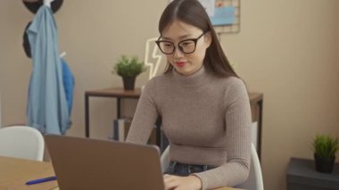 Genç Asyalı bir kadın dizüstü bilgisayarı üzerinde özenle çalışıyor, sakin ve modern bir ev ortamında..