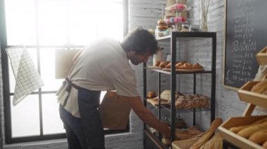 Fırında çalışan genç bir adam sıcak ve kapalı bir ortamda raflarda taze ekmek paketliyor.