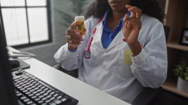 Afrika kökenli Amerikalı kadın doktor elleri açık bir şekilde klinikte otururken bir şişe hap gösteriyor..