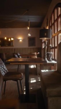 Sıcak bir şekilde aydınlatılmış, içi boş bir kafe ahşap masalar, deri sandalyeler ve ortam aydınlatması..
