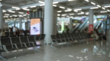 Bulanık insanların ve oturma alanlarının bulunduğu bir havaalanı terminalinin odaklanmamış görüntüsü, hareketli seyahat ortamının bokeh etkisini yakalıyor.