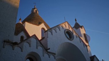 Alberobello 'daki güzel kilise kuleleri, alacakaranlıkta altın güneş ışığıyla aydınlatılan puglia belirgin konik çatılar ve derin mavi gökyüzüne karşı beyazlatılmış duvarlar sergiliyor..
