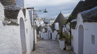 Alberobello, puglia, İtalya 'da pitoresk bir sokak sahnesi geleneksel beyaz trulli evleri ve bulutlu bir gökyüzünün altında tuhaf bir kaldırım taşı yolu..