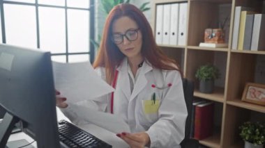 Beyaz laboratuvar önlüklü, kızıl saçlı genç bir kadın, kapalı klinik işyerindeki belgeleri incelerken gözlüğünü çıkarıyor..