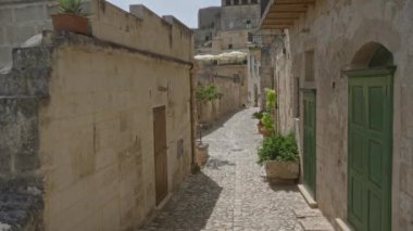 Materya, Basilicata, İtalya 'da dar bir kaldırım taşı sokak. Çevrede tarihi taş binalar, yeşil kapılar ve saksı bitkileri var..