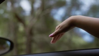 Güneşli bir günde, huzurlu bir açık hava gezisinde arabanın camından dışarı sallanan boyalı tırnaklı bir kadın eli.