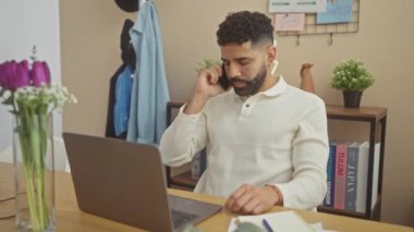 Evde dizüstü bilgisayarla çalışan yakışıklı İspanyol bir adam ve bir telefon görüşmesi yapıyor.