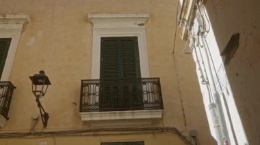 Gelibolu, Puglia, İtalya 'da dar bir sokakta pencereleri, balkonları, demir parmaklıkları ve parlak güneş ışığı altında klasik bir sokak lambası olan eski bir bina var..
