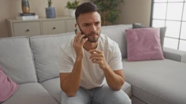 Oturma odasında sakallı İspanyol bir adam oturmuş, akıllı telefon kullanırken hayal kırıklığını dile getiriyor..