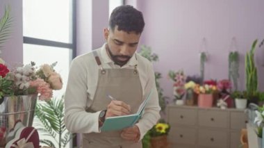 Sakallı genç bir İspanyol, çiçekçi dükkanında renkli çiçeklerle dolu notlar yazıyor..