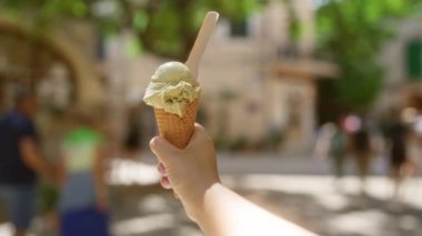 Ağaçlı bir dondurma külahını tutarken ve açık havada güneşli bir günde arka planda insanları bulanıklaştırırken