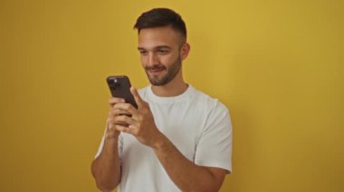 İspanyol asıllı genç adam başarıyı ve zaferi akıllı telefonla kutluyor, heyecanlı ve gururlu sarı arka plan, zafer için kolunu kaldırdı.