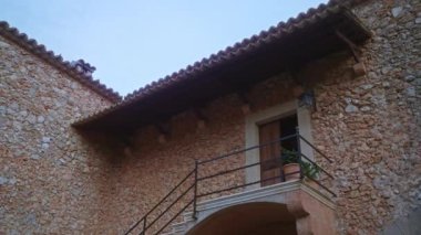 Korkulukları ve saksısı olan taştan bir evin ön cephesinde, temiz gökyüzünün altında taşralı bir balkon.