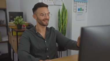 Ofis odasında elleri ve arka planda rafları olan Latin asıllı genç bir adam dinleniyor.