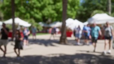 Bulanık bir pazar yerinde güneş ışığı altında Mallorca 'da ağaçlarla yürüyen insanlar.