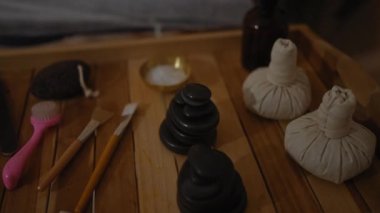 Masaj taşları, temel yağlar ve ahşap tepside fırçalar gibi sağlıklı aksesuarlarla kaplıca odasında dinlenen bir kadın, kapalı alanda huzurlu, sakin ve rahatlatıcı bir atmosfer yaratıyor.