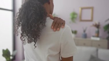 Kıvırcık saçlı Afrikalı genç bir Amerikalı kadın, ev bitkileri ve çağdaş dekorlarla dolu şık bir oturma odasında dikilirken omzuna dokunuyor..