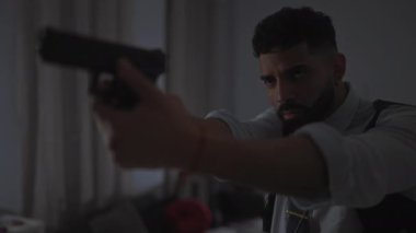 Sakallı bir adam, yoğun bir odak, gerginlik ve potansiyel tehlike içeren bir tabancayı içeri doğrultuyor..